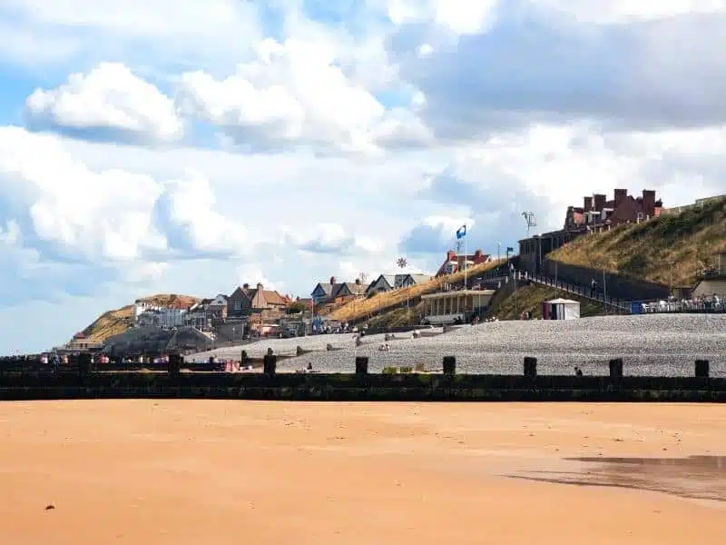 sandy and pebbly beach with wooden groynes in front of a small clifftop town