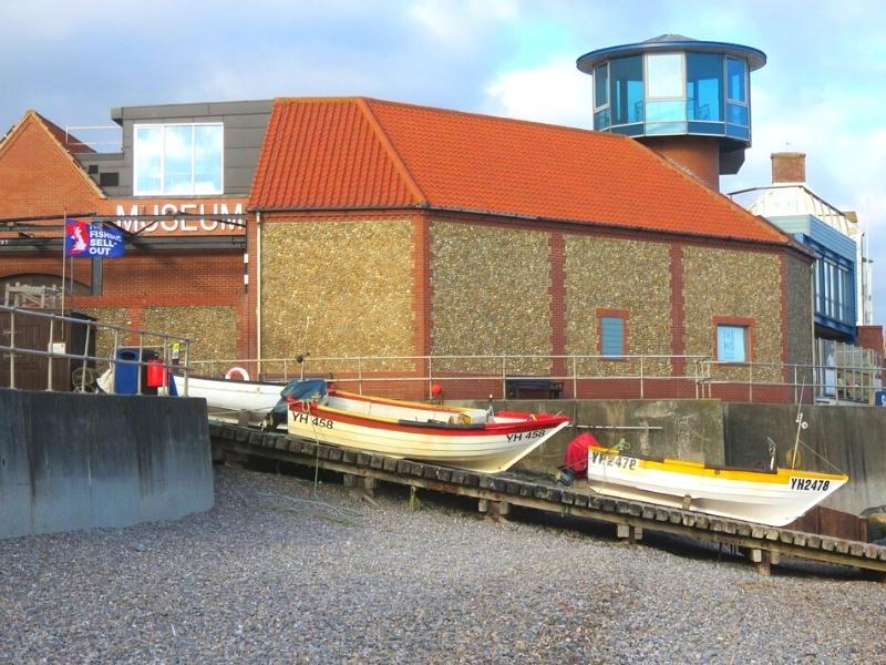 red roofed flint building with boats on a slipway and a glass round tower