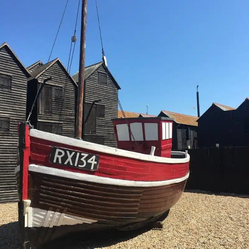 red white and brown wooden boat on shingle in front of black fishermans huts