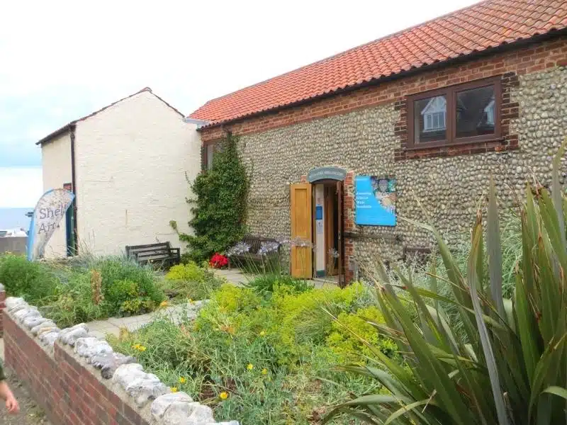 brick and flint building with plants in a front garden behind a brick wall