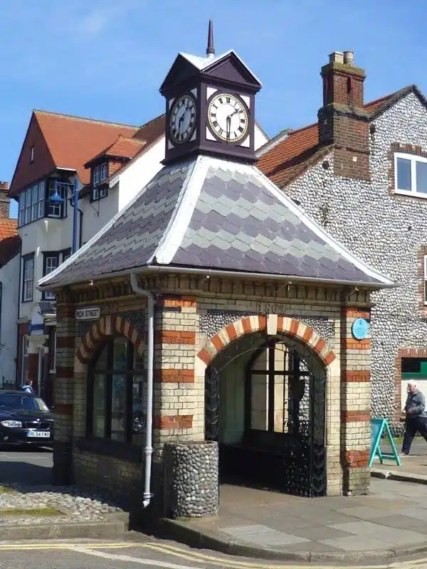 small clock tower over arched building with a blue plaque