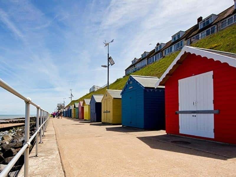 brightly painted wooden beach huts on a promenade with railings