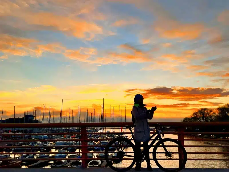 Woman standing on a bridge with a bike looking at the sunset