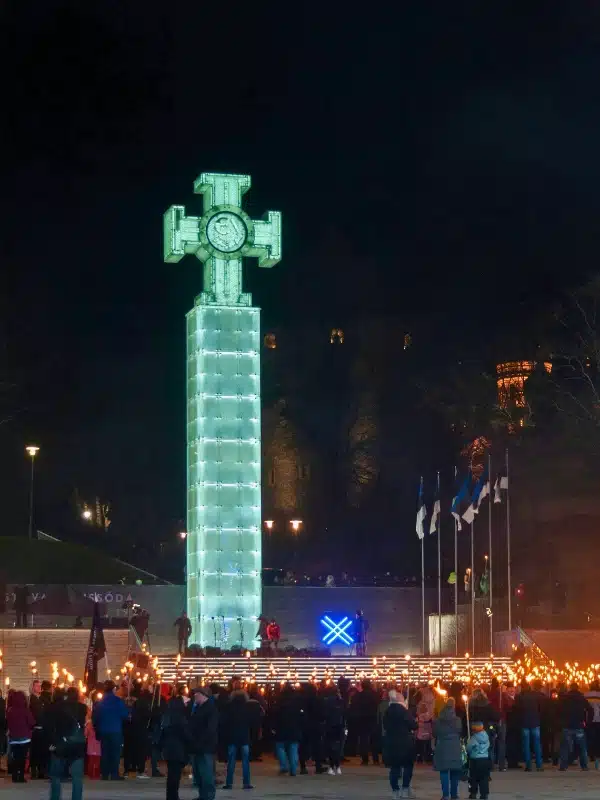 large victory column with a cross on top lit up at night with people on the steps at the front holding torches