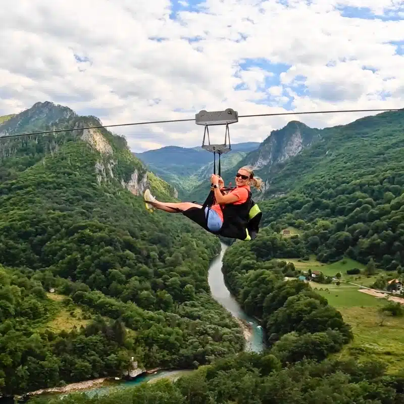 woman in an orange t-shirt riding a zipline over a river canyon