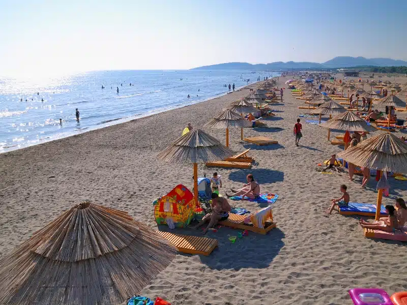 long sandy beach lined with beach beds and umberella and people in the water