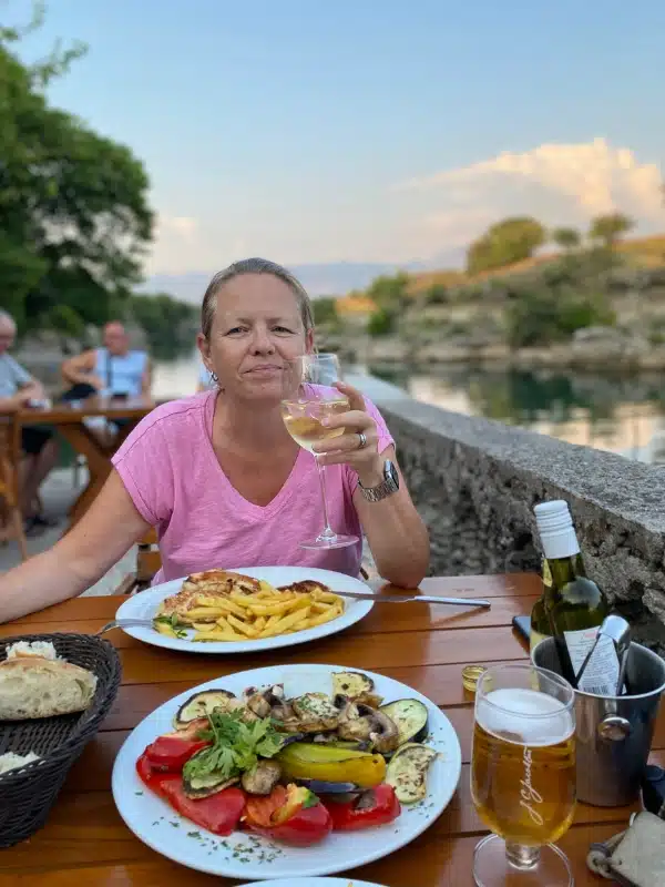 woman wearing a pink tshirt holding a glass of wine with plates of food on a table