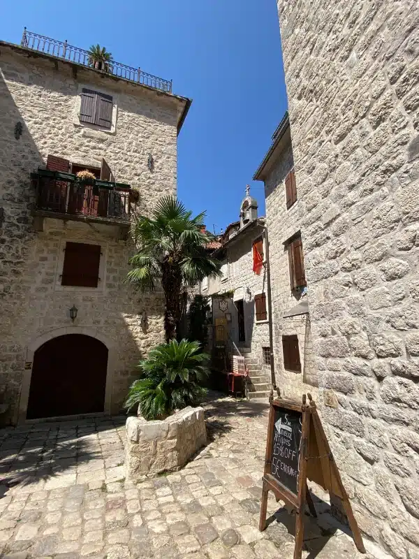 stone houses around a small courtyard with a palm tree and blackboard