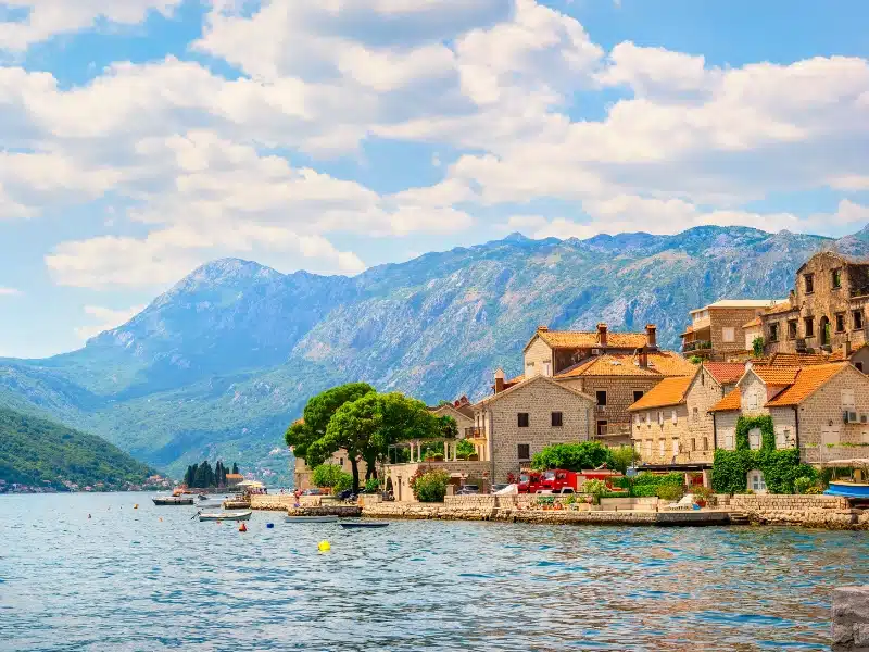 lakeside village of stone houses with terracotta roofs and mountains in the distance