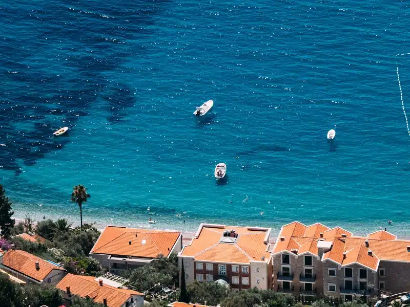 tiny stretch of beach with turquoise water seen over terracotta roofed buildings