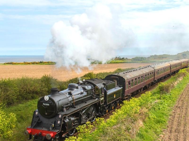 steam train puffing through flat fields with the sea in the distance