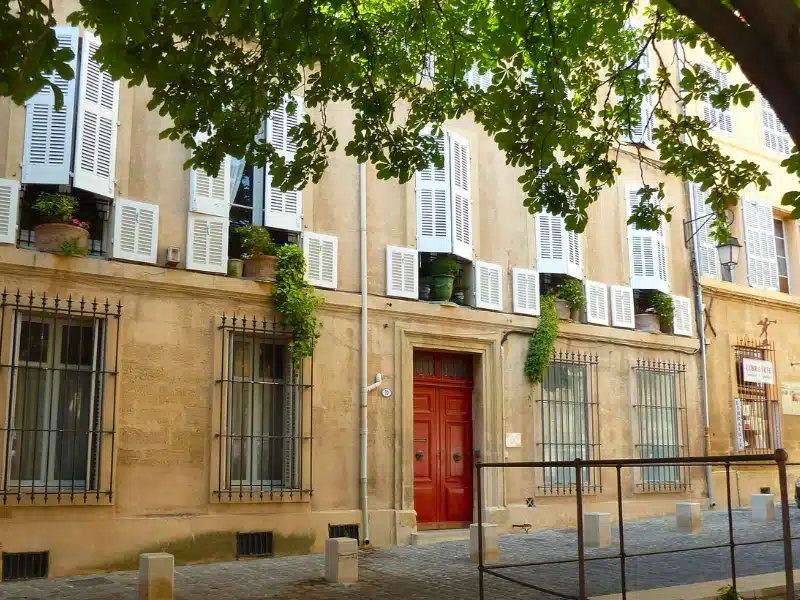 Cream colored stone building with a red door and white shutters