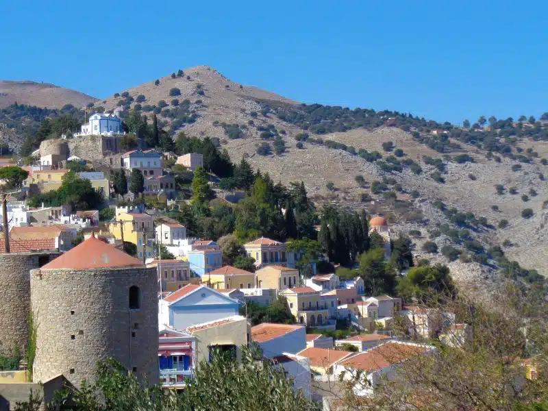 round stone towers with red conical roofs against white and pastel painted houses along a hillside
