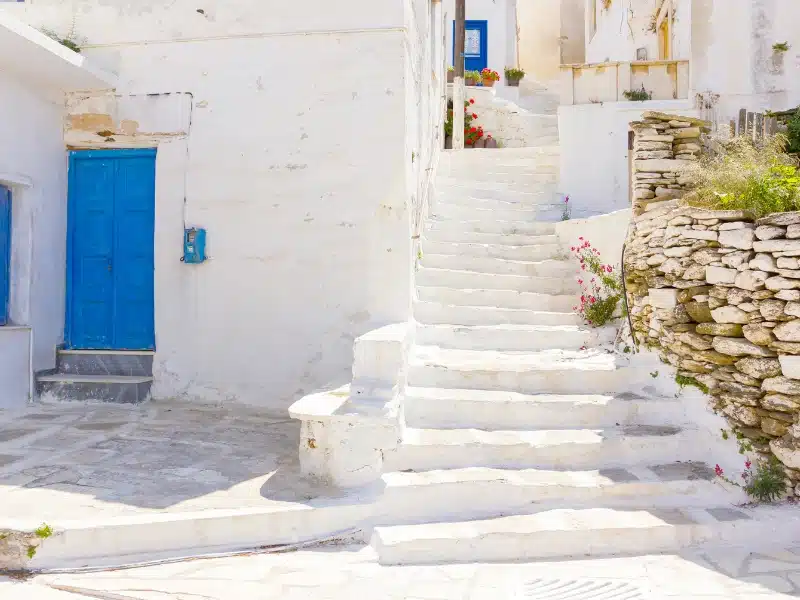 Traditional white painted street with steps against a stone wall and blue painted doors