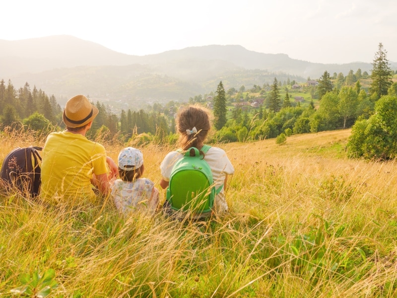 Young family sitting in nature with view over trees to mountains 