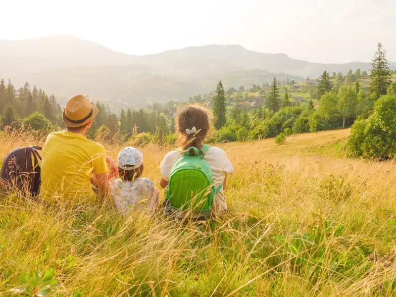 Young family sitting in nature with view over trees to mountains 