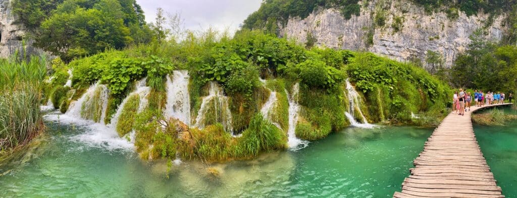 multiple small waterfalls cascade through vegetation with a wooden boardwalk passing by