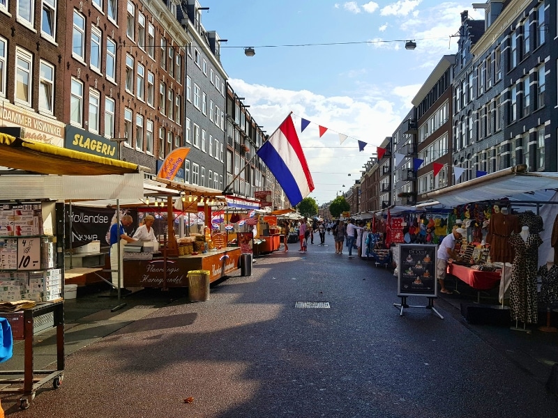street lined with tall houses and market stalls, with a Dutch flag waving