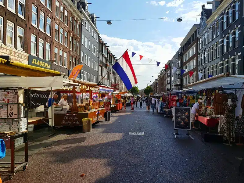 street lined with tall houses and market stalls, with a Dutch flag waving