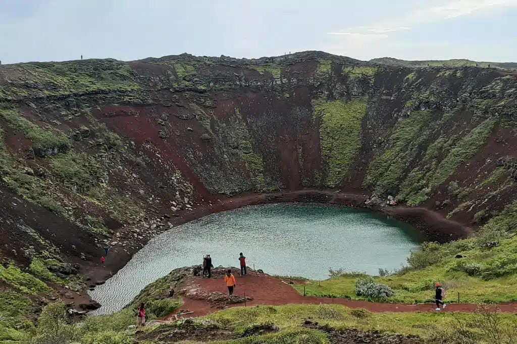 Poeple looking into a red and green volcanic crater filled with water