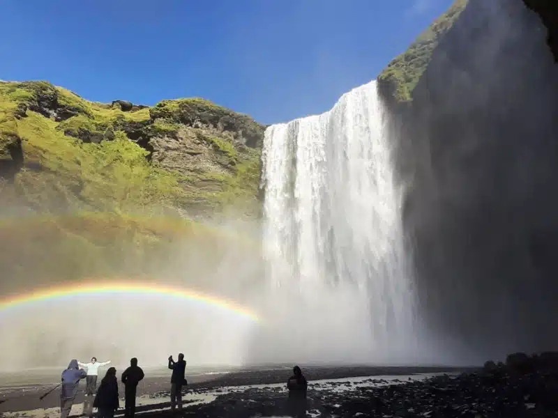 People taking photographs of a large waterfall and rainbow