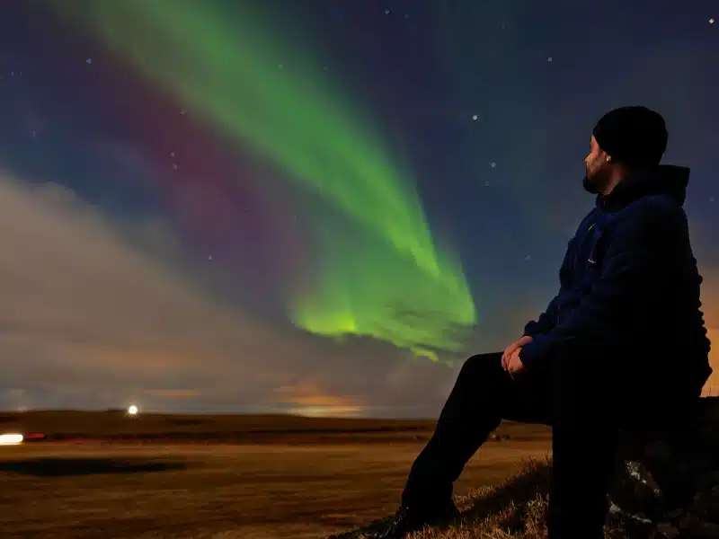 Traveller appreciating northern lights and admiring magical nordic phenomenon, man under icelandic starry night sky looking at aurora borealis. 