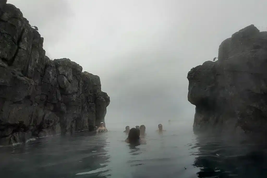 People swimming in a rocky geothermal pool withi steam rising