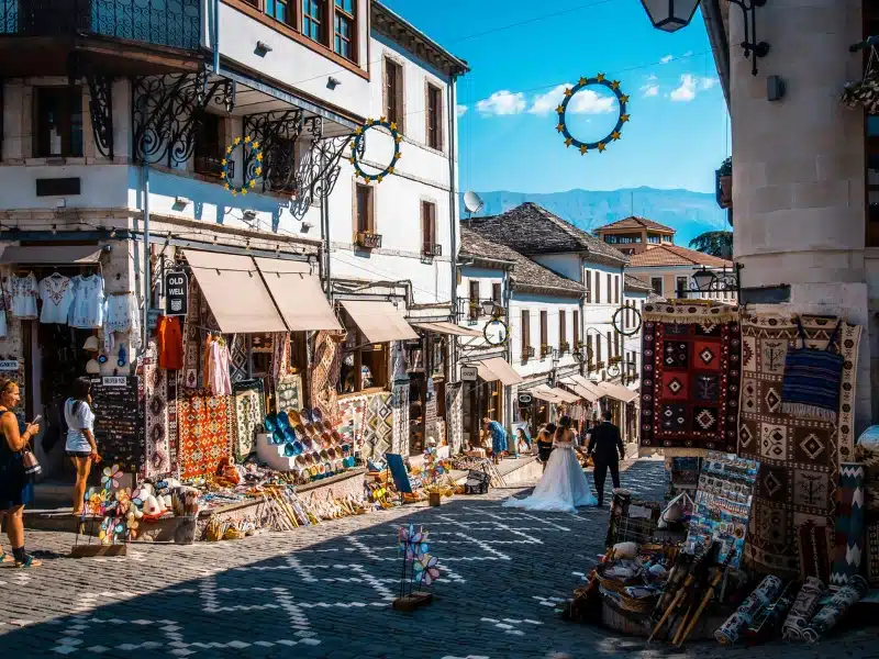 black and white cobbled street lined with shops and cafes with rugs and wares on display