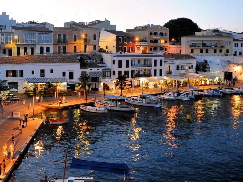 a view of a harbor at dusk with boats in the waterand bars along the water front