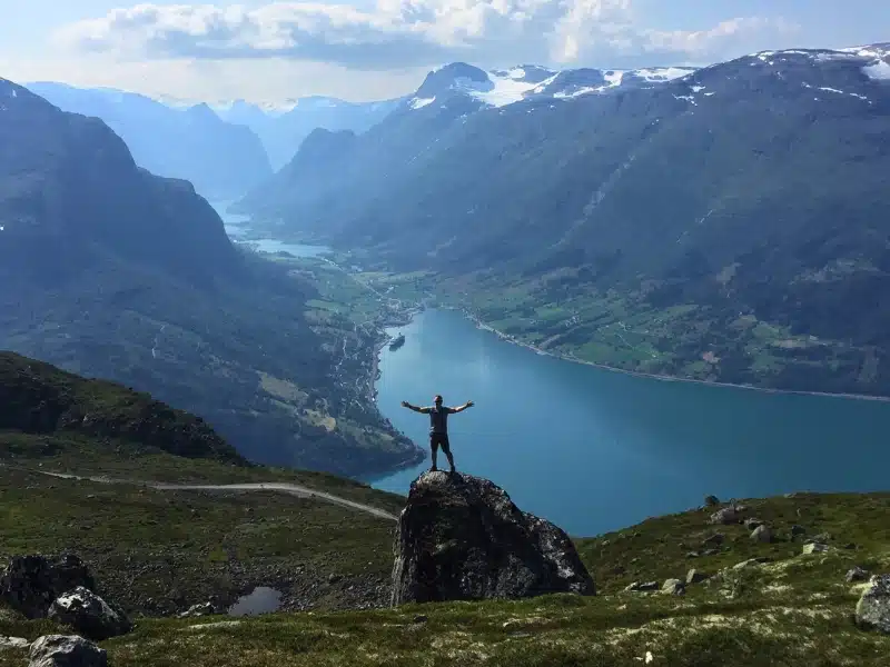 Man standing on a rock in front of a Norwegian fjord with mountains in the distance