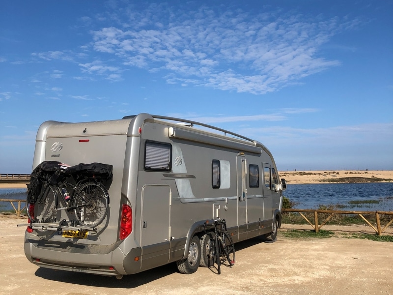 silver motorhome parked in front of a lagoon with sandy beaches