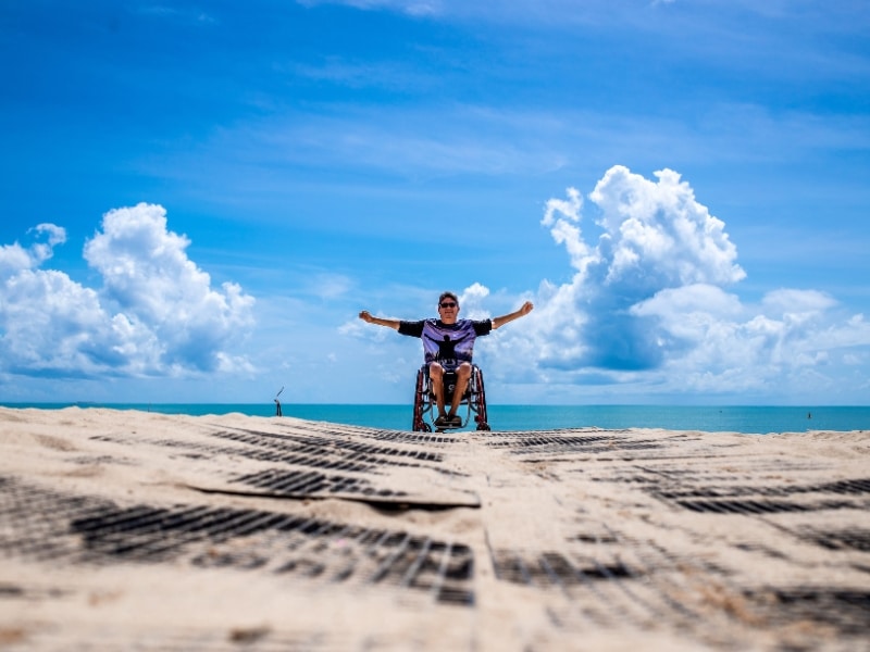 person in a wheelchair on a beach with arms stretched wide