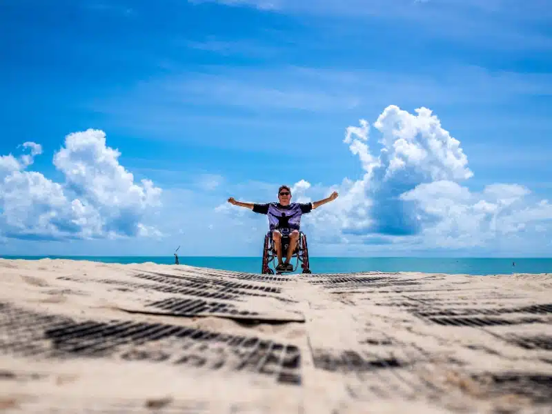 person in a wheelchair on a beach with arms stretched wide