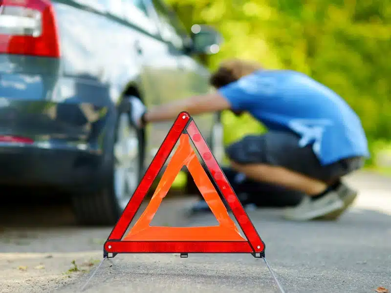 man in a blue top looking at a car tyre with a warning triangle on display