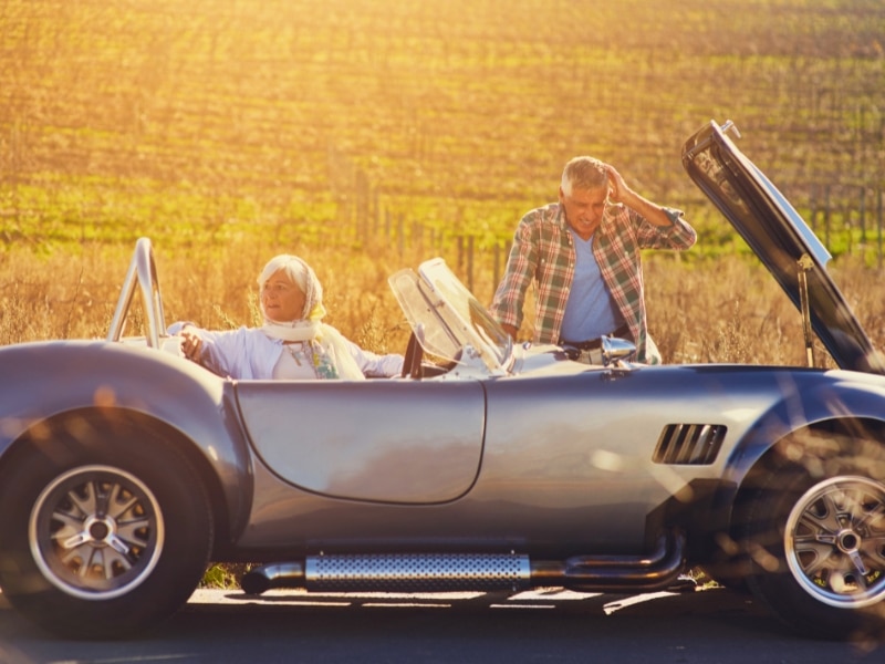 Car and problem by road with man doing engine check and woman waiting in the car