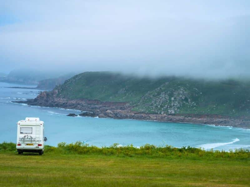 campervan parked in a grassy field overlooking a sea cover on a misty day