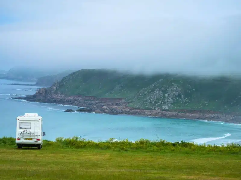 photo-1534517535933-e38e7658663f campervan parked in a grassy field overlooking a sea cover on a misty day