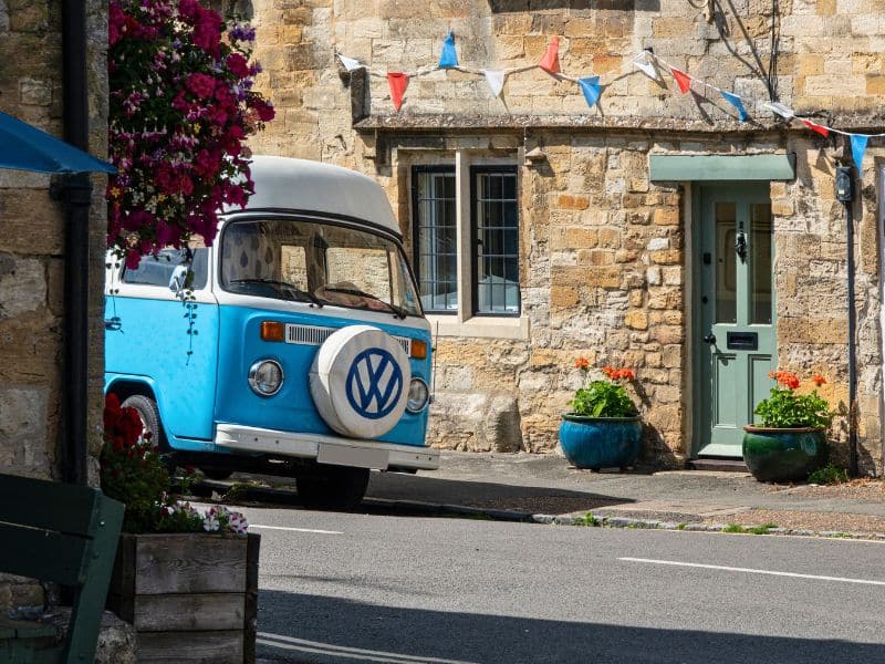 Blue and white campervan parked in front of an historic stone cottage