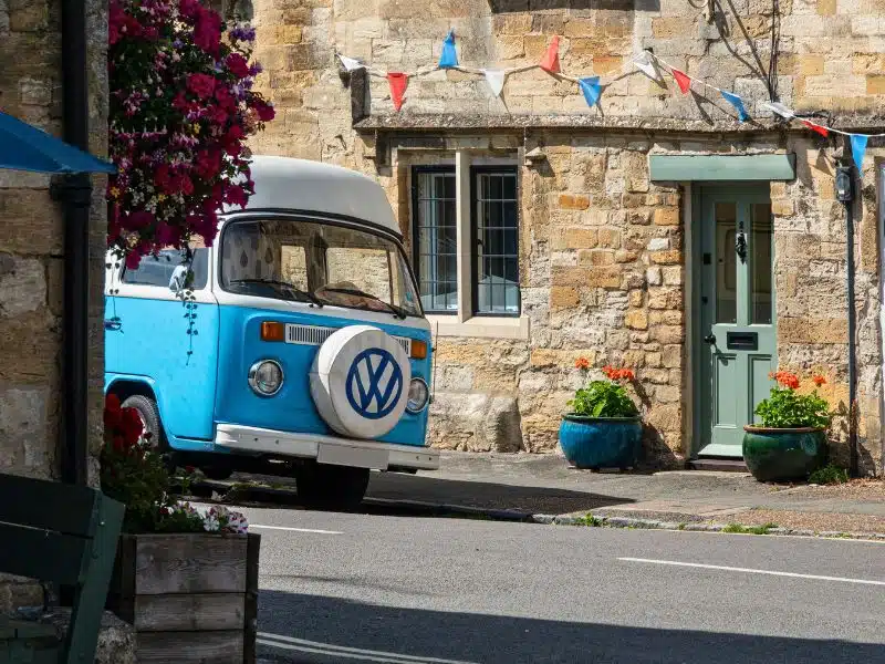 Blue and white campervan parked in front of an historic stone cottage