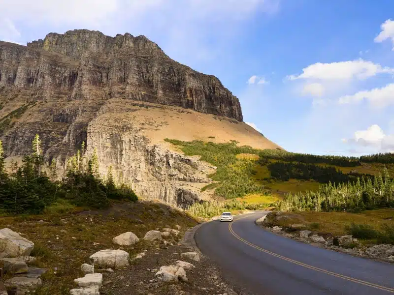 A lone white car makes a curve under the tall peaks of the Rocky Mountains