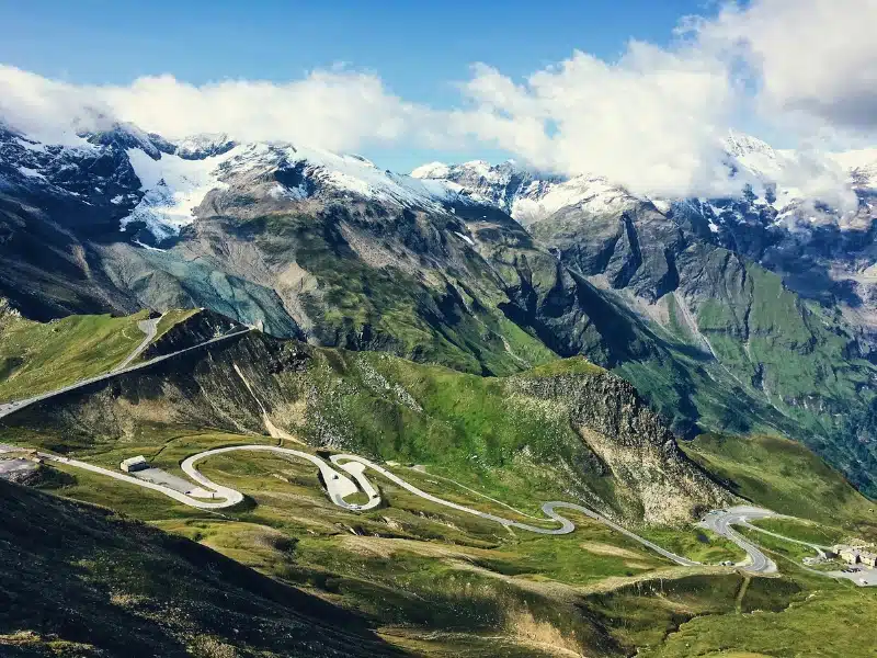Tarmac road winding through snow capped mountains and alpine meadows