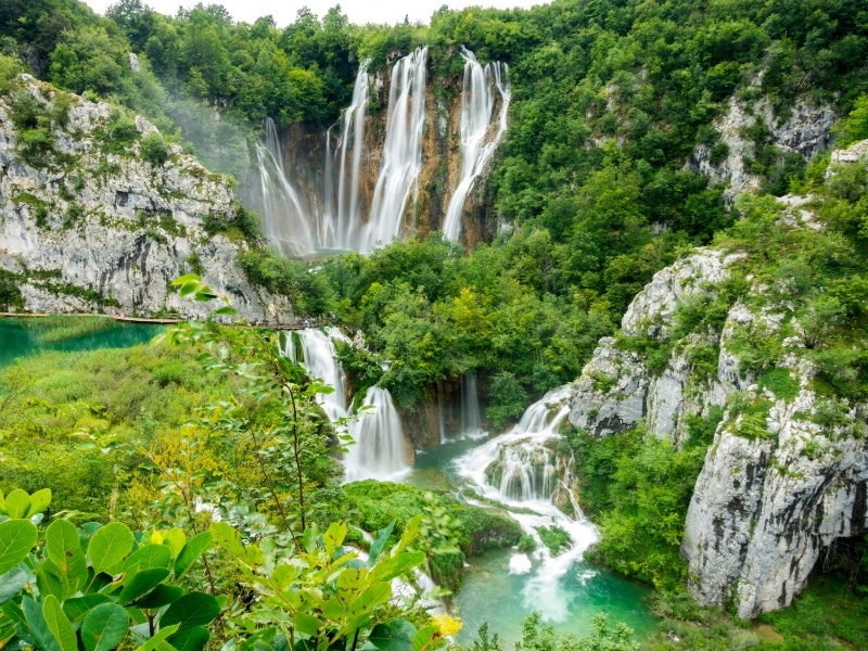 multiple high waterfalls cascading intto a lake below and surrounded by foliage