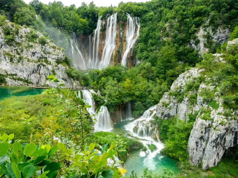 multiple high waterfalls cascading intto a lake below and surrounded by foliage