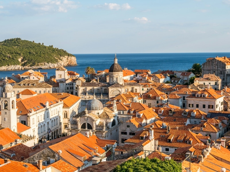 City of creamy stone buildings, domes and statues with a foreground of bushes and trees