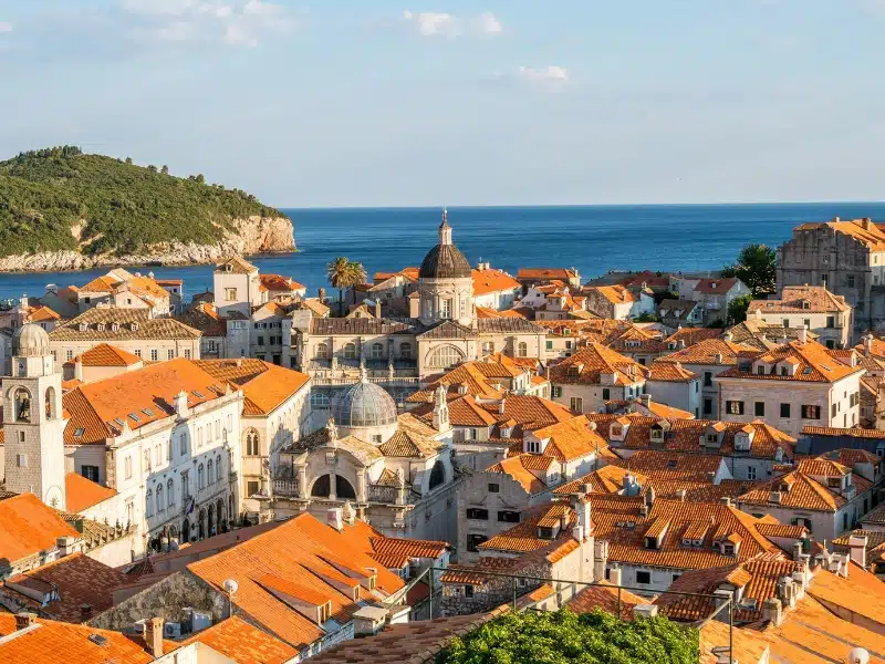City of creamy stone buildings, domes and statues with a foreground of bushes and trees