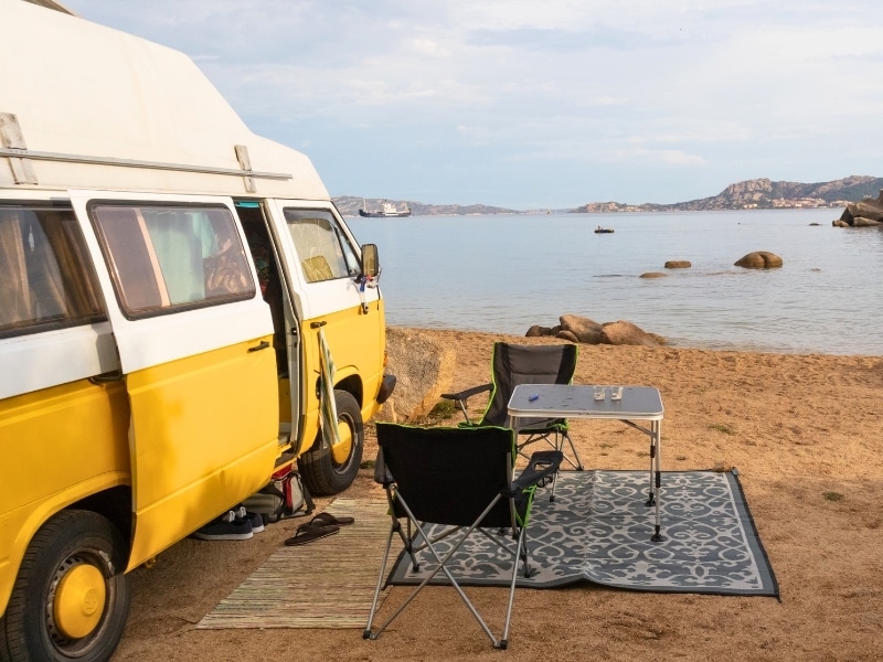 Old colorful retro camper van on camping site at beautiful rocky coastal landscape of Costa Smeralda, north east Sardinia, Italy.