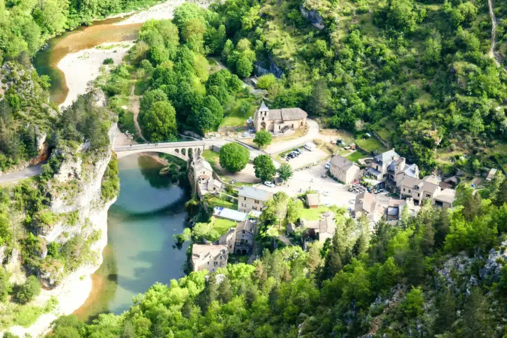 small stone village with buildings and a church on a river bank with a bridge