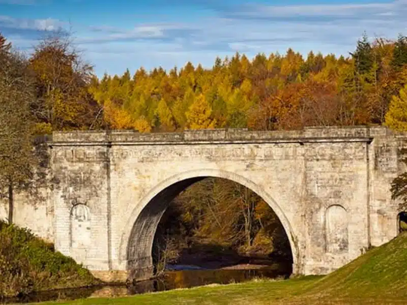 Stone bridge in a country park with trees showing their autum colors