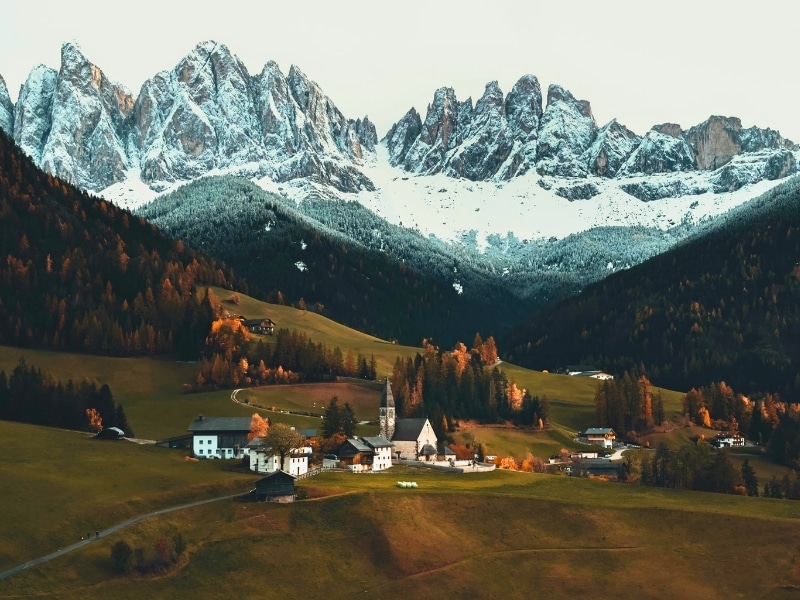 Italian valley with a small village of white houses and a church at atumn with snow on the distant mountains