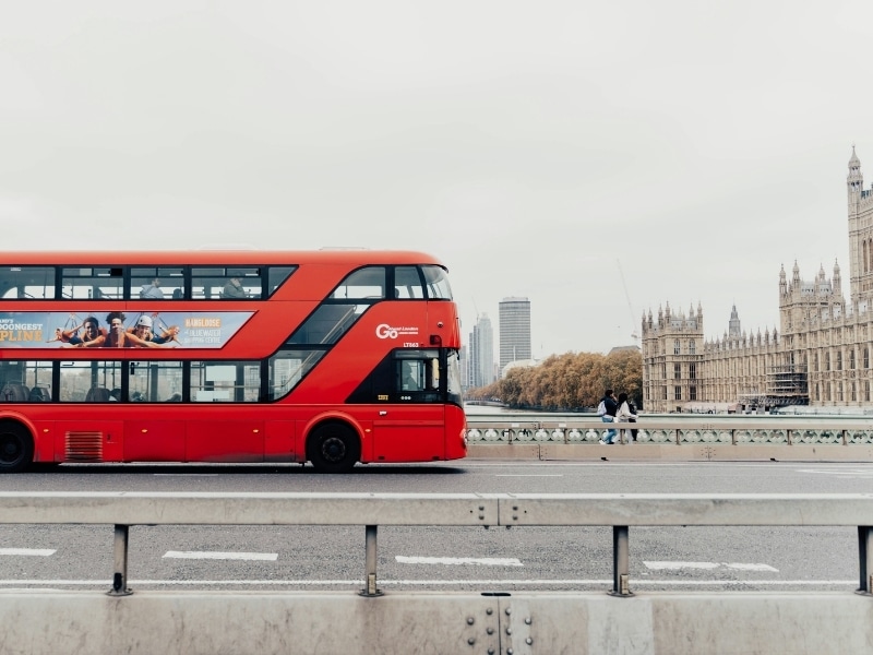 red bus on a bridge with historic buildings in the background